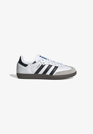 Biały sneaker Adidas Samba z czarnymi paskami, szarą zamszową czubkiem, czarną naszywką na pięcie oraz białymi sznurowadłami na białym tle.