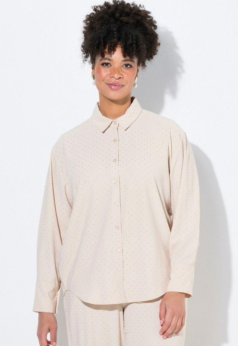 Blusa beige chiaro con bottoni anteriori, maniche lunghe e un sottile motivo a pois. Presenta un colletto classico e una texture di tessuto morbido.