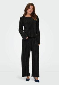 Ensemble à deux pièces noir plissé comprenant un haut à manches longues et un pantalon à jambes larges. Texture douce avec une coupe décontractée. Accentué par des manches allongées.