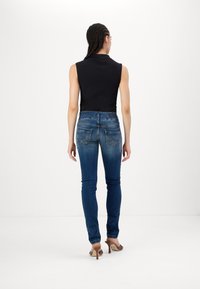 Top negro sin mangas ajustado combinado con jeans ajustados azules que presentan bolsillos traseros y ligeros desgastes, llevados con sandalias de tacón marrones.