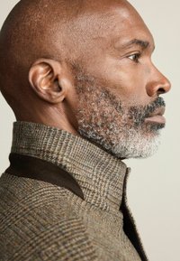 Pruun houndsstooth müts, millel on kõrge krae ja tumedad sametaktsentid, omades tekstuuriga kangast ja lähedalt sobivat disaini.