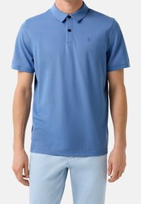 Polo bleu à manches courtes en tissu lisse, avec une patte de boutonnage à trois boutons et un logo discret de la marque sur la poitrine gauche.