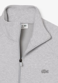 Giacca grigia con zip realizzata in tessuto misto cotone. Presenta un colletto alto, bordi a coste e un piccolo logo sul lato sinistro del petto.