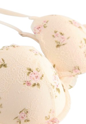 Reggiseno con pizzo in morbido beige con motivi floreali rosa. Presenta coppe sagomate e spalline regolabili per il supporto. Tessuto strutturato.