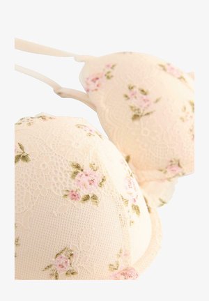 Reggiseno con pizzo in morbido beige con motivi floreali rosa. Presenta coppe sagomate e spalline regolabili per il supporto. Tessuto strutturato.