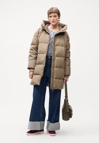 Puffer jacket in beige with a hood, featuring a quilted design. Paired with wide-leg denim jeans with frayed cuffs and burgundy sneakers.