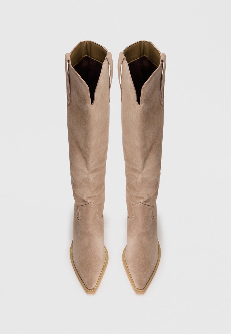 Botas altas de ante beige hasta la rodilla con punteras afiladas y costuras decorativas. Cuentan con un diseño de corte en la parte superior y una suela de goma ligera.