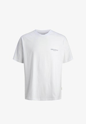 Garçon souriant portant une casquette beige, un t-shirt blanc avec le texte "ORIGINALS", un jean large délavé et des baskets blanches, debout sur un fond blanc.
