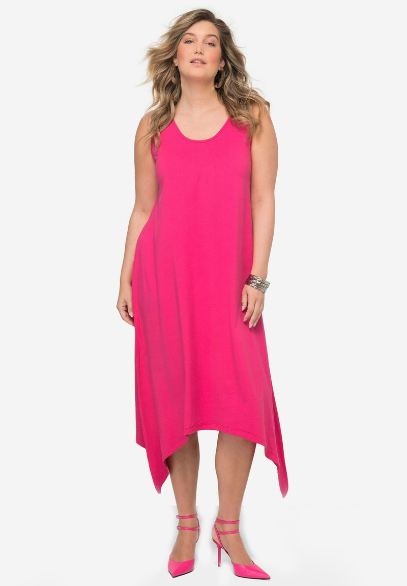 Abito senza maniche fucsia con orlo irregolare e spacchi laterali, realizzato in tessuto leggero. Abbinato a scarpe con tacco alte rosa coordinato.