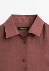 Rød linnedskjorte med knap-til-krave, to knapper og et mærke med "Massimo Dutti." Tekstureret, letvægtsstof.