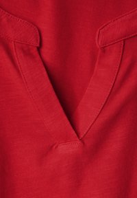 Roter Stoff mit V-Ausschnitt-Design; mit kontrastierenden Kragenakzenten; glatte Textur mit leichtem Glanz. Maßgeschneiderte Steppnähte.