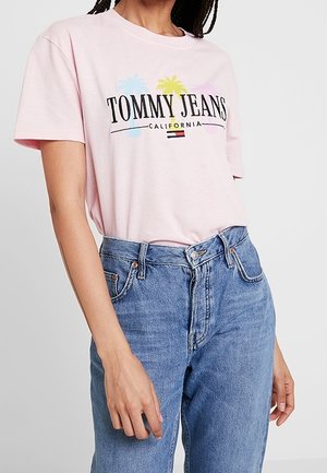 Różowa bawełniana koszulka z krótkimi rękawami, z logo "TOMMY JEANS CALIFORNIA" oraz grafiką palm, w połączeniu z niebieskimi dżinsami z wysokim stanem.