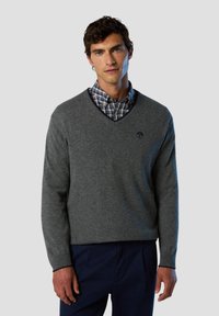 Maglione grigio a scollo a V realizzato in tessuto morbido, con una finitura testurizzata e un piccolo logo sul lato sinistro del petto, abbinato a una camicia a quadri sottostante.