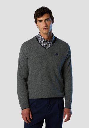 Maglione grigio a scollo a V realizzato in tessuto morbido, con una finitura testurizzata e un piccolo logo sul lato sinistro del petto, abbinato a una camicia a quadri sottostante.
