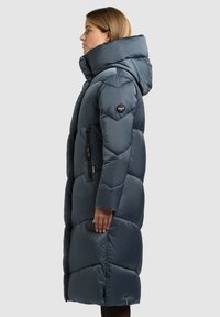 Pikk, paks, tumel sinine mantel, millel on kapuuts, tõmblukuga taskud ja peal nähtav tikandiga voodriga pehme, läikiv tekstuur.