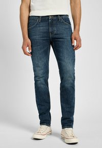 Jeans de denim azul de corte slim, con un lavado medio, diseño de cinco bolsillos, que presentan un desvanecimiento sutil, costura en contraste y una cinturilla estándar.