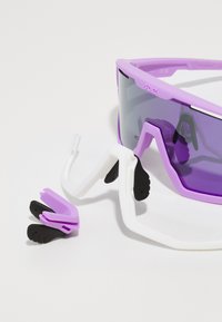 Sport solbriller med lilla ramme, grå gradient linser og avtakbare hvite armer. Inkluderer ekstra lilla og svarte neseputer.