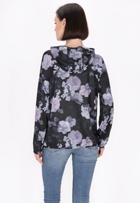 Giacca nera con cappuccio, a maniche lunghe, con un motivo floreale. Realizzata in tessuto morbido, presenta fiori viola chiaro su uno sfondo scuro.