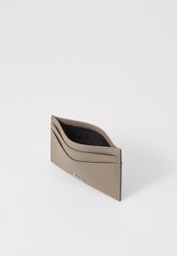 Beige läder kortfodral med texturerad yta, som har flera fack och en subtil logotypdetalj på framsidan. Kompakt och strömlinjeformad design.