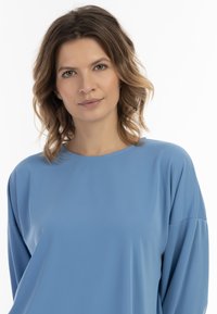 Világoskék, hosszú ujjú felső, puha és sima anyagból. Lazán illeszkedő fazon, kerek nyakkivágással, kissé ejtett vállakkal.