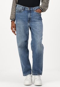 Lyseblå denimjeans med rett benpassform, fem lommer, knappelukking og lett falming. Brukt med hvite sneakers.