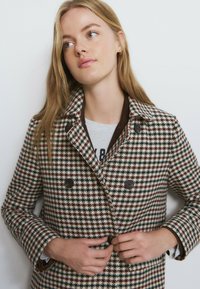 Abrigo cruzado con estampado de pata de gallo que presenta tonos marrones, crema y verdes. Botones marrones destacados y un cuello de contraste.