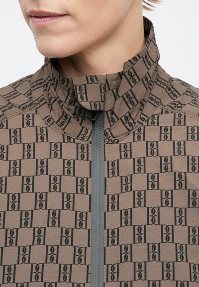 Jachetă maro cu guler înalt, cu un model geometric negru. Închidere frontală cu fermoar și accente gri. Material neted și texturat.