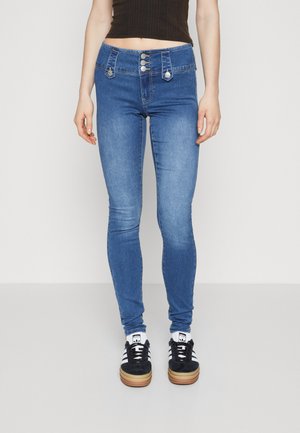 Skinny blue jeans with a high waistband, featuring three metal buttons, contrasting stitching, and a smooth denim texture. Paired with black sneakers.