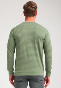 Sudadera verde con un patrón geométrico, de manga larga, cuello redondo y puños acanalados. La tela parece suave y tiene un acabado texturizado.