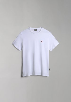 Camiseta de algodón blanca con mangas cortas y cuello redondo, que presenta un pequeño logo rojo y azul en el lado izquierdo del pecho y una etiqueta en el costado.