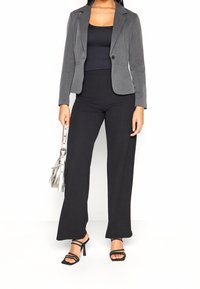 Šedý upravený blazer přes černý top a černé široké kalhoty. Modelka drží stříbrnou kabelku a má na sobě černé sandály na vysokém podpatku. Jednoduchý a moderní design.