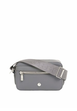 Sac bandoulière rectangulaire gris avec poche zippée à l'avant, tirette de zip argentée et large bandoulière réglable embossée du nom de la marque "LACOSTE".