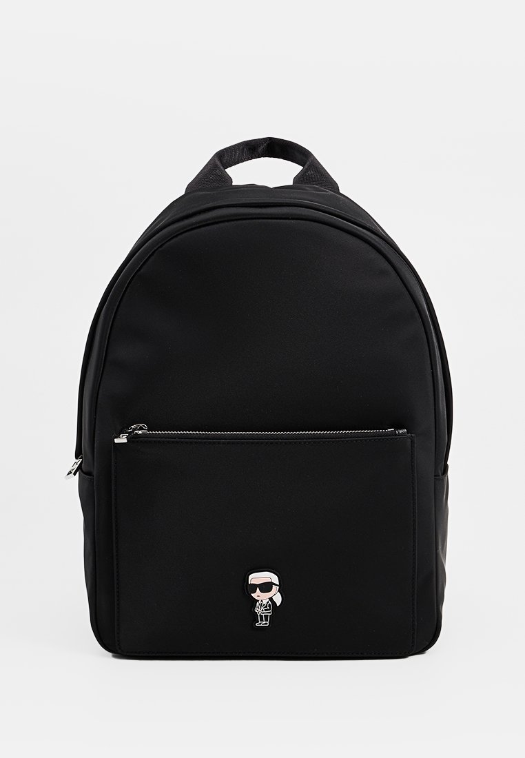 Sac à dos en nylon noir de forme arrondie, avec une poche avant zippée et un emblème de personnage de dessin animé en bas. Texture lisse.