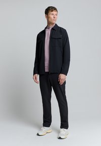 Marineblauwe ritsjack met twee borstzakken over een lichtroze pullover, gecombineerd met zwarte broek en witte sportschoenen. Zachte stof textuur.