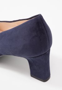 Chaussure à talon haut en suede bleu marine avec un bout rond et un talon bloc. Texture lisse et détails de coutures le long du bord supérieur.