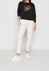 Sudadera negra con un logo triangular y acentos de purpurina, combinada con pantalones cremosos con estampado y zapatillas blancas.