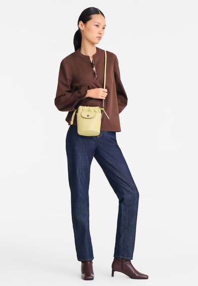 Brown long-sleeve top with a round neck, dark blue jeans, and a small light yellow drawstring bag. Model wears brown ankle boots.