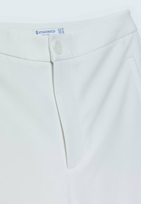 Ceinture de pantalon blanche avec fermeture par bouton, braguette zippée, poche latérale et étiquette de marque Stradivarius visible avec les détails de la taille.