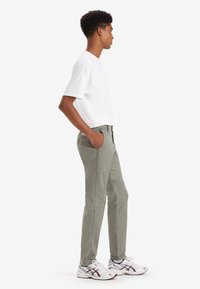 Pantalones de algodón grises con corte recto, que cuentan con bolsillos laterales y un pequeño parche de logo; combinados con una camiseta blanca de manga corta y zapatillas.