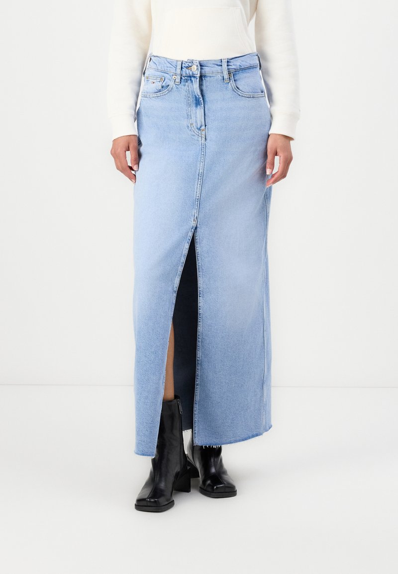 Light blue denim maxi skirt with a front slit, belt loops, and five-pocket design. Paired with black ankle boots.