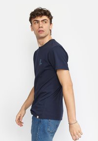 Marineblauwe katoenen T-shirt met korte mouwen, ronde halslijn en klein tekstlogo op de borst. Standaard pasvorm, gladde textuur en geen zichtbare patronen.