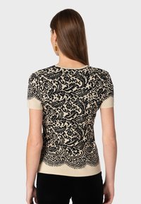 Jersey de manga corta en negro y crema con un intrincado diseño de paisley y dobladillo ondulado, hecho de una suave tela de punto texturizada.