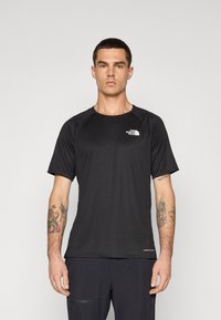 Camiseta atlética preta de manga curta com um tecido texturizado, gola redonda e logótipo no peito, usada com calças escuras.