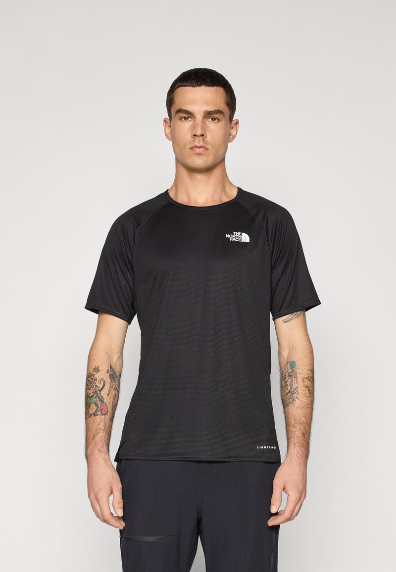 Camiseta atlética preta de manga curta com um tecido texturizado, gola redonda e logótipo no peito, usada com calças escuras.