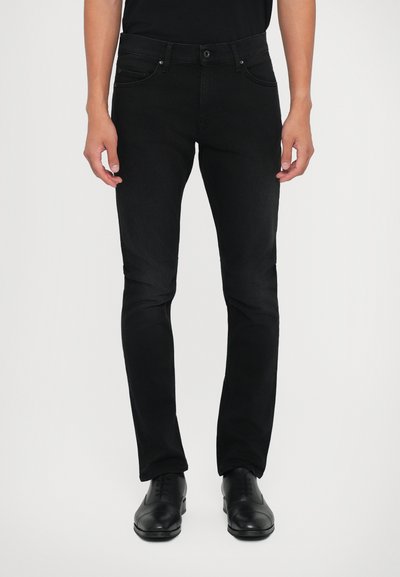Czarne dżinsy o slim fit, pięć kieszeni, z klasycznym zapięciem na guziki, zestawione z czarnymi eleganckimi butami.