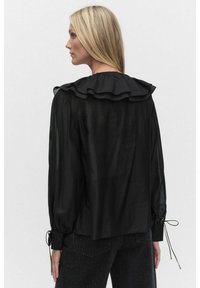 Svart blus med volangkrage, långa ärmar med knytningar och en genomskinlig textur, visad bakifrån.