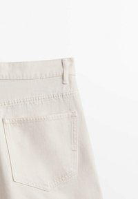 Vue arrière d'un jean en denim beige clair montrant la ceinture, la boucle de ceinture et une poche arrière unique sur fond blanc.