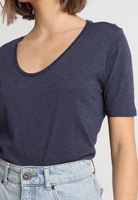 Námořnická modrá tričko s krátkým rukávem a širokým kulatým výstřihem, vyrobené z měkké tkaniny; nošené s světlými džínovými šortkami s vysokým pasem.