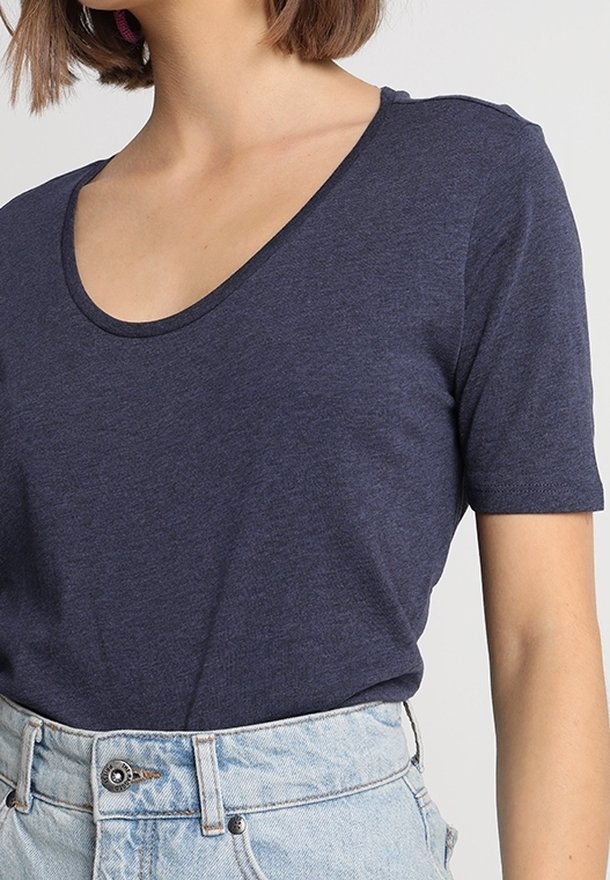 Námořnická modrá tričko s krátkým rukávem a širokým kulatým výstřihem, vyrobené z měkké tkaniny; nošené s světlými džínovými šortkami s vysokým pasem.