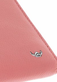Esquina de producto de cuero rosa con textura visible, acentuada por un pequeño logo plateado que presenta un diseño de cuerno estilizado.